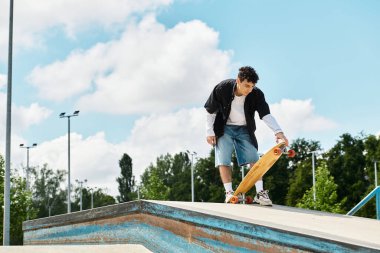 Enerjik genç adam kaykayın üzerinde dengede duruyor, canlı bir parkta rampadan kaymaya hazır..