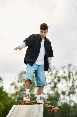 Genç bir adam parktaki kaykayında dengede duruyor ve arka plandaki yeteneklerini sergiliyor..