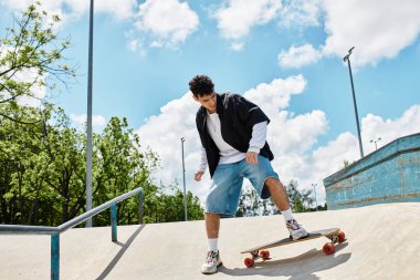 Genç bir adam parktaki parlak mavi gökyüzünün altında kaykay numaralarını yapıyor.