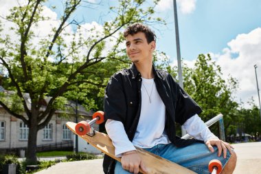 Genç bir adam parkta güzel bir ortamda kaykayıyla oturarak biraz dinlenir..