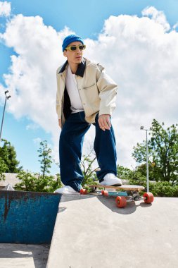 Genç bir adam, canlı bir park ortamında hareketlenmeye hazır bir kaykay üzerinde özgüvenle dengede duruyor..