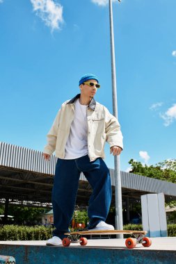 Moda kıyafetli bir adam parktaki parlak mavi gökyüzünün altında sörf tahtasına biniyor..