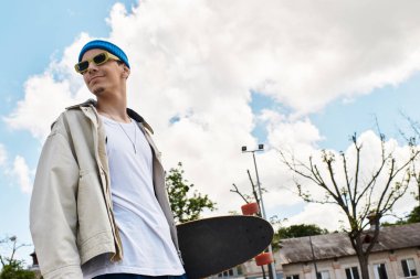 Genç bir adam güvenle parkta duruyor, rahat giyinmiş ve kaykay seansına hazır..