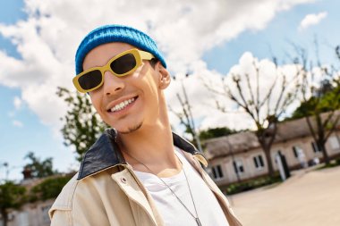 Genç adam yeşilliklerle çevrili canlı bir parkta güneşli havanın tadını çıkarırken ışıl ışıl gülümsüyor..