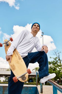 Genç bir adam kaykayıyla kendine güvenerek ayakta duruyor, parlak bir parkta güneşi emiyor..