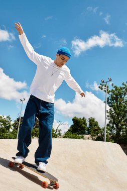 Genç bir adam kaykay yeteneklerini güneşli bir parkta, kabarık bulutlu gösteriş yapıyor..