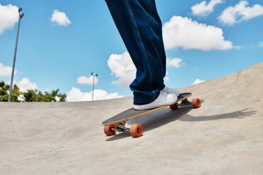 Genç bir adam açık mavi gökyüzünün altındaki canlı bir parkta kaykayını ustalıkla sürüyor..