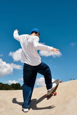 Enerjik genç adam parkta güneşli bir günün tadını çıkarırken kaykay numarası yapıyor..