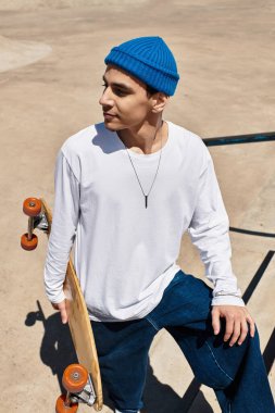 Genç bir adam parkta, elinde kaykayla, rahat bir şekilde poz veriyor..