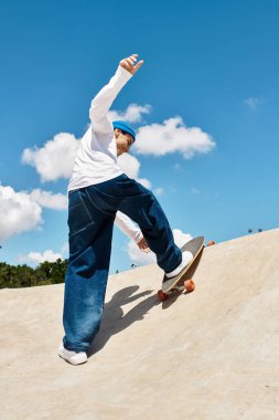 Genç bir adam açık mavi gökyüzü olan canlı bir parkta kaykay yeteneklerini sergiliyor..