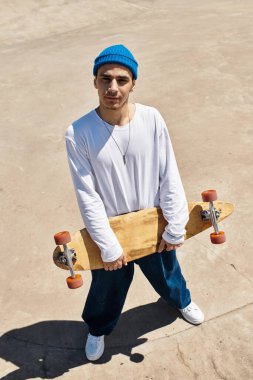 Sıradan giyinmiş genç bir adam parkta kaykayla duruyor, neşe ve enerji saçıyor..