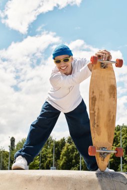 Günlük kıyafetli gülümseyen adam güneşli bir parkta kaykay yeteneğini gösteriyor..