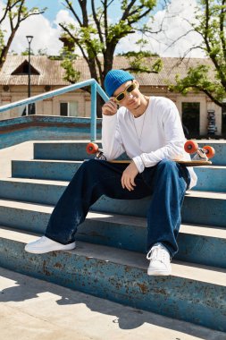 Genç bir adam parkın merdivenlerinde kaykayla güneşli ve güneşli bir günün tadını çıkarıyor..