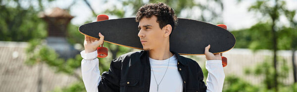 Молодой человек уверенно стоит в парке, держа скейтборд, готовый к приключениям.