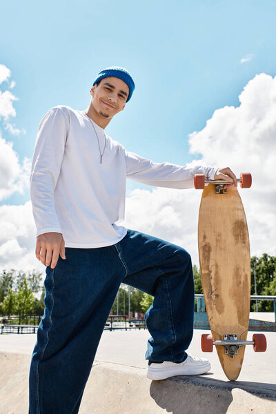 Веселый молодой человек гордо стоит у парка, держа свой скейтборд под ярким небом.