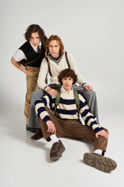 Üç genç adam eşsiz moda tarzlarını sergiliyor, canlı bir stüdyoda güven içinde poz veriyorlar..