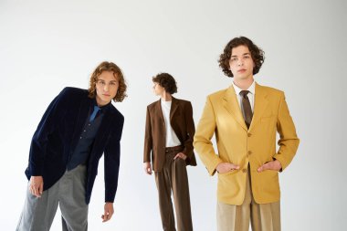 Üç genç adam benzersiz tarzlarını canlı takım elbiseler ve kapalı mekanlarda kendilerine güvenen pozlarla ifade ediyorlar..