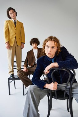 Üç genç adam içeride yaratıcı bir şekilde poz verirken eşsiz moda tercihlerini sergilerler..