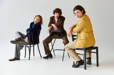 Üç modaya uygun genç adam, benzersiz stillerini ve dostluklarını vurgulayarak koltuklara güven içinde poz veriyor..