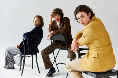 Üç modaya uygun genç adam, minimalist bir arka plana karşı özgüvenle poz veriyor..