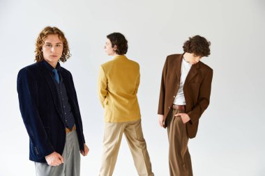 Parlak bir stüdyoda poz verirken üç adam kendi tarzlarını özgüvenle ifade eder..