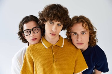 Üç şık genç adam özgüvenle poz veriyor, eşsiz stillerini ve arkadaşlıklarını sergiliyorlar..