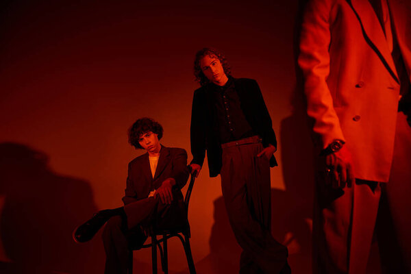 Two young men display their unique fashion sense in a striking, warm lit setting.