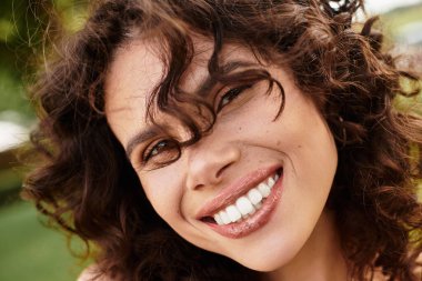 Parlak güneş ışığı, yeşilliğin ortasında şık giyinmiş neşeli genç bir kadını aydınlatıyor..