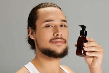 Yakışıklı genç sakallı adam, elinde bakım ürünleri, stilini ve kişisel bakımını sergiliyor..