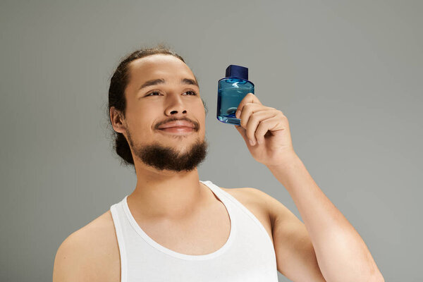 Очаровательный молодой человек улыбается, держа синюю бутылку аромата в стильной студии.