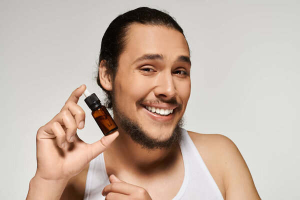Handsome young man with a beard holds up a bottle of essential oil, radiating joy and positivity.