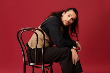 Sakallı yakışıklı genç adam sıradan bir sandalyede oturuyor ve kendine has moda anlayışını sergiliyor..