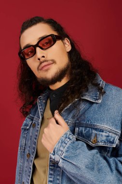Sakallı ve şık güneş gözlüklü yakışıklı genç adam kot ceketiyle rahatça poz veriyor..