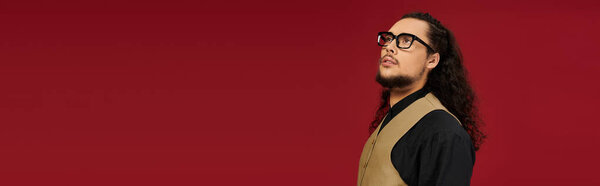 Бородатый молодой человек в очках созерцает современную моду на красном фоне.