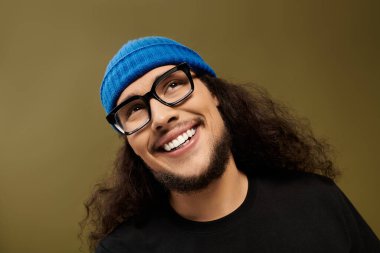 Sakallı yakışıklı genç adam mavi bir bere ve siyah bir gömlek giyerken neşeyle gülümsüyor..
