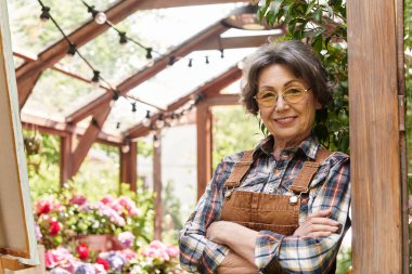 Neşeli, son sınıf öğrencisi bir kadın çiçeklere ve bitkilere olan sevgisini kucaklayarak gururla bahçesinde duruyor..