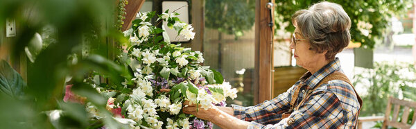 In a lush garden, a lovely senior woman carefully arranges a colorful bouquet of fresh flowers.