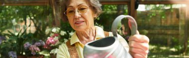 Zarif yaşlı bir kadın, güneşin altında açan çiçekleri sularken bahçesinde neşe topluyor..