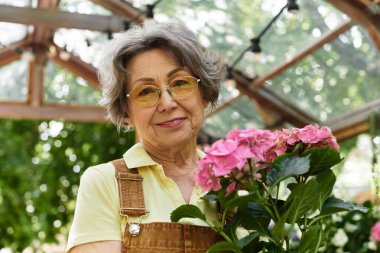 Güzel, son sınıf öğrencisi bir kadın, huzurlu bir bahçede renkli çiçeklerle ilgilenerek vakit geçirmekten zevk alır..