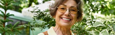 Neşeli, yaşlı bir kadın yemyeşil bahçesiyle çevrili bahçesinde sıcacık gülümsüyor..