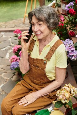 Güzel, son sınıf öğrencisi bir kadın renkli çiçeklerin arasında otururken telefonda sıcak bir sohbet eder..