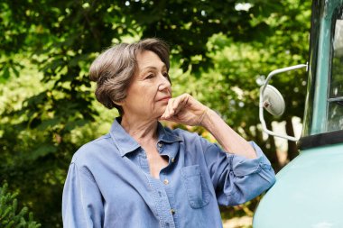 Güzel, son sınıf öğrencisi bir kadın, çiçeklerle dolu bahçesinde, eski bir arabanın yanında düşünceli bir şekilde duruyor..
