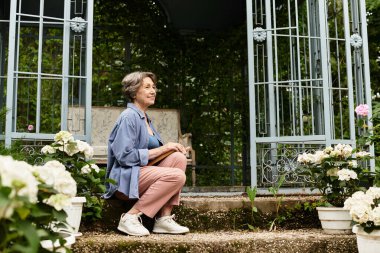 Huzurlu bir bahçede, güzel bir son sınıf kadını huzur içinde oturur, güzelliğin tadını çıkarır..