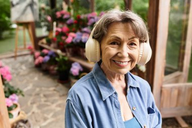 Canlı bir bahçede, son sınıf öğrencisi bir kadın müziğin tadını çıkarırken neşeyle gülümsüyor..