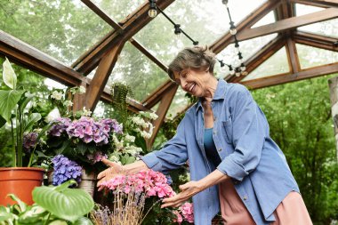 Güzel, son sınıf güzeli kadın güzel bahçesindeki vahada renkli çiçeklerle mutlu bir şekilde etkileşim içinde.