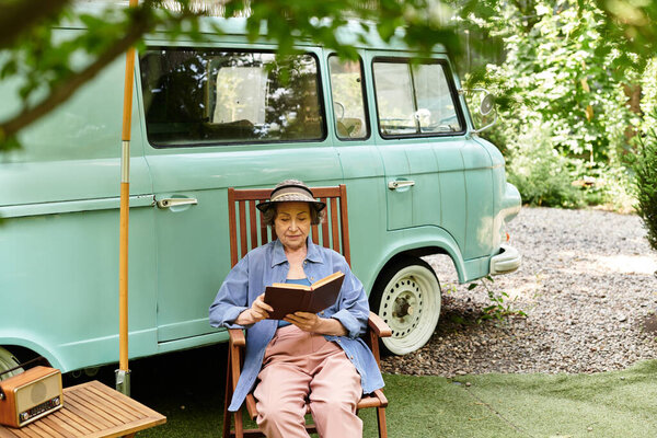 Старшая женщина расслабляется в саду, читая книгу винтажного фургона.