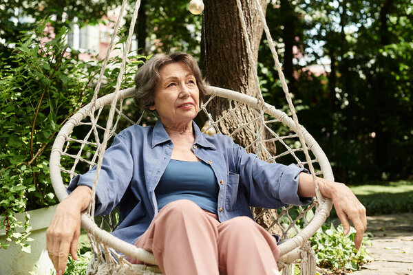 A serene senior woman relaxes on a garden swing amid lush greenery and sunlight.
