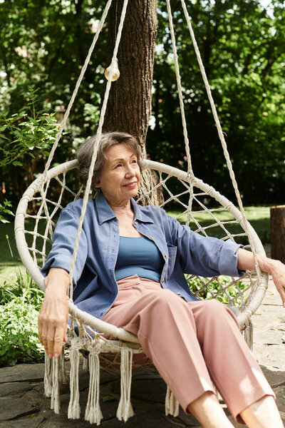 A beautiful senior woman relaxes in a cozy swing, surrounded by lush greenery and vibrant flowers.