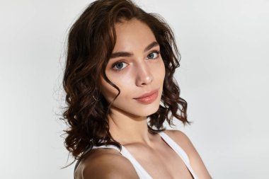 Göz alıcı makyajlı genç bir kadın stüdyoda gri bir zemine karşı zarifçe poz veriyor..