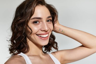 Güzel bir kadın stüdyoda poz veriyor, çarpıcı makyajını ve neşeli ifadesini vurguluyor..